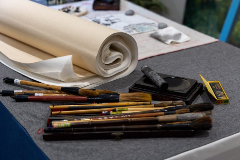 A roll of paper, Chinese brushes and ink stick laid haphazardly on a table covered with a dark grey cloth
