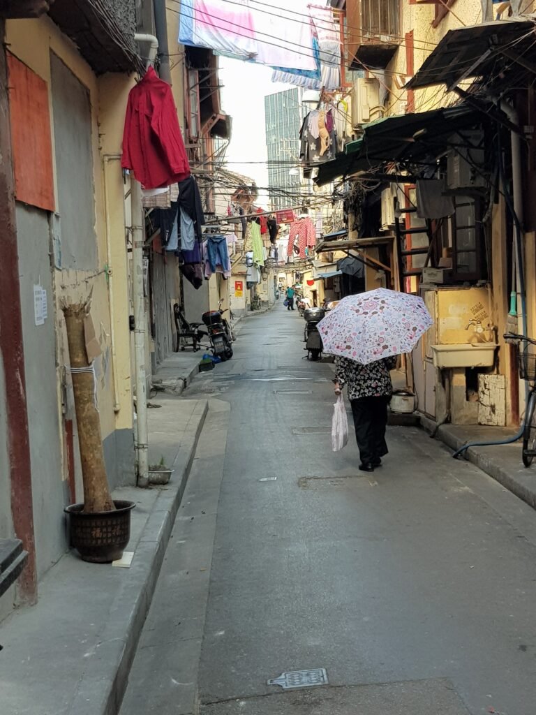 Woman with umbrella walking down a narrow alley in old Shanghai, washing hanging out from houses looking onto the alley