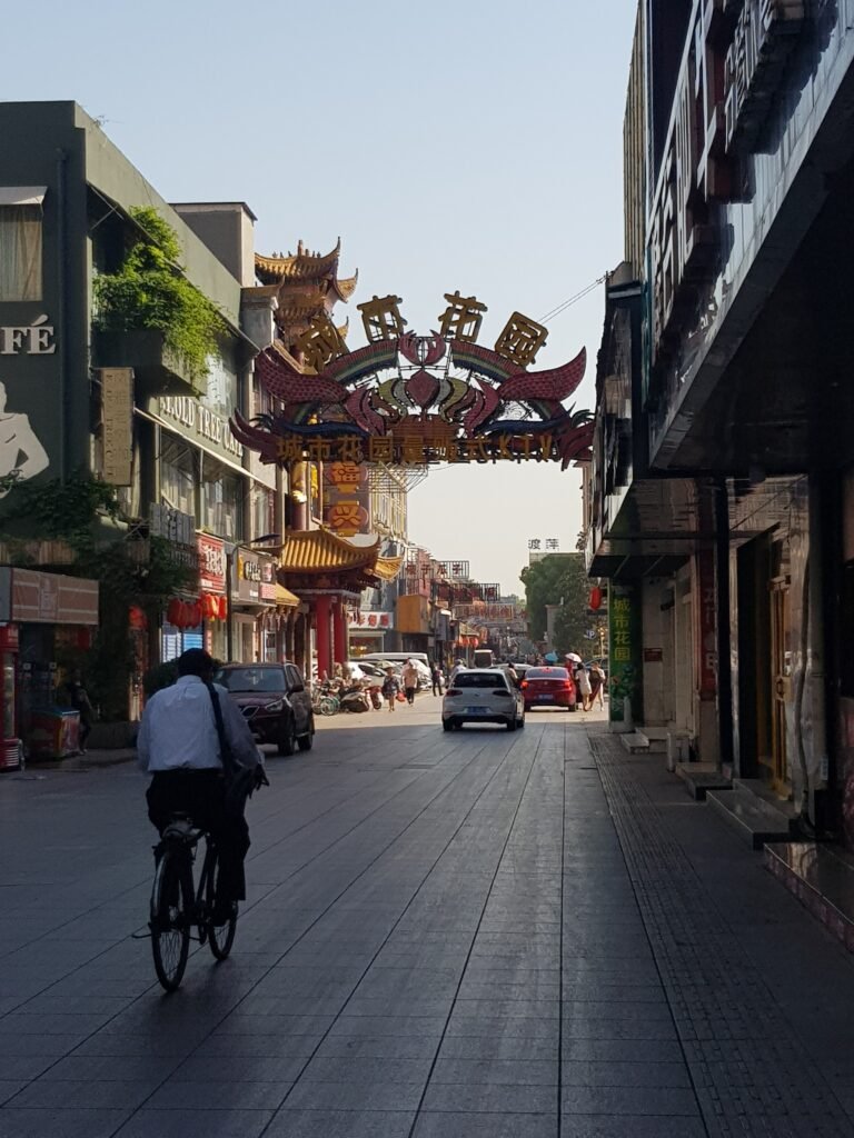 Looking down Gourmet street, Wuhu, which is lined with restaurants, the sun recently risen on the horizon. The street is empty of people except a man on a bicycle in the foreground