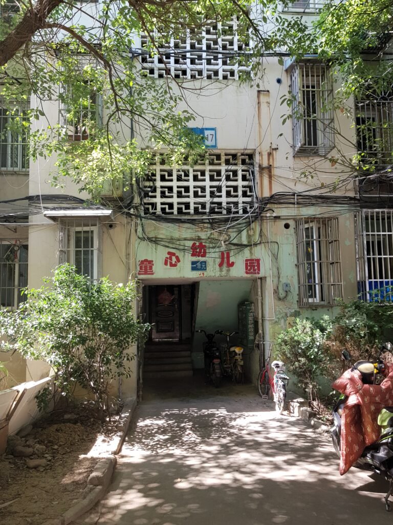 A path shaded with trees, leading towards an entrance to an apartment block in the Chinese city of Wuhu. Above the entrance is an inscription in red Chinese script