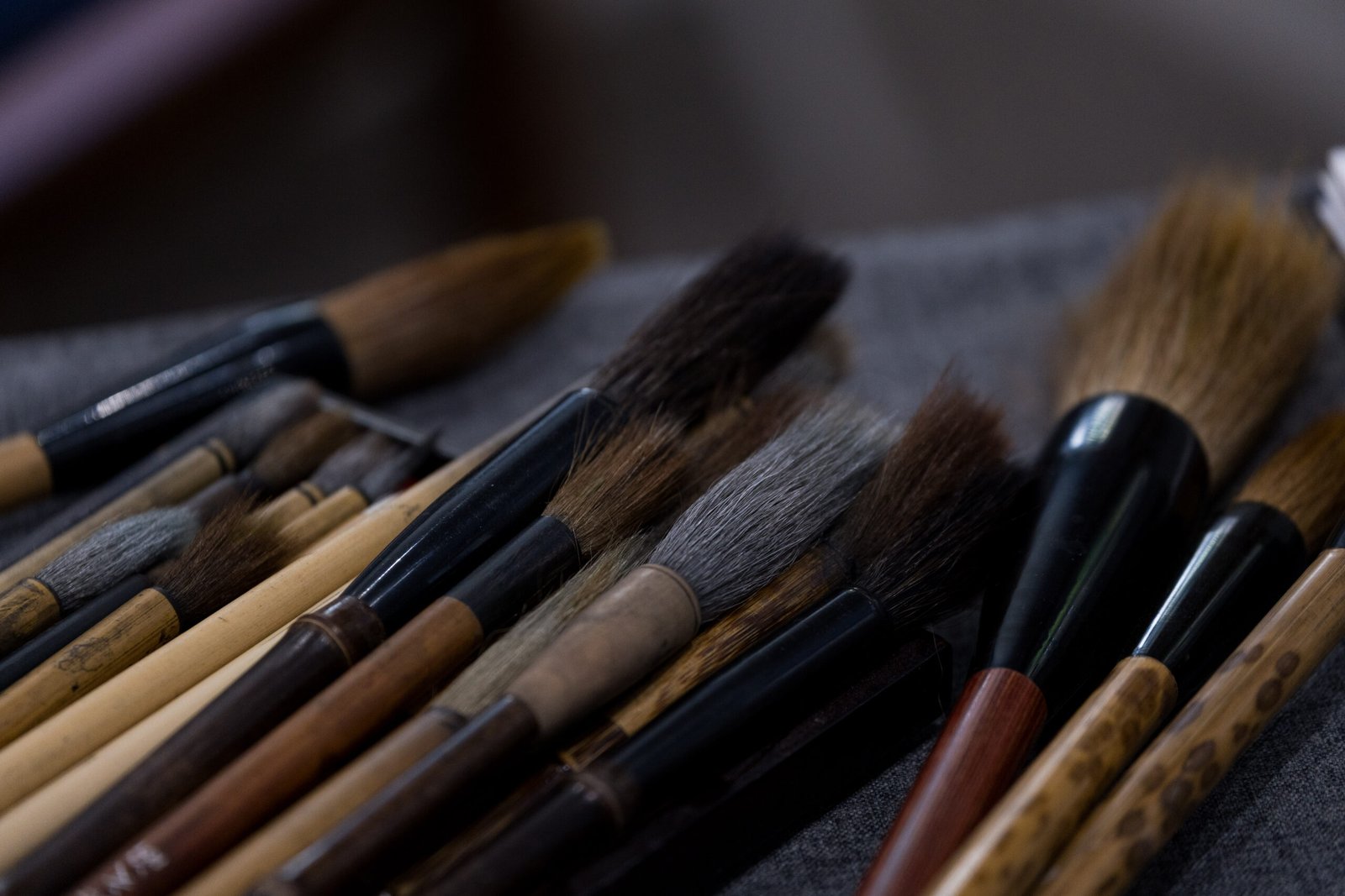 A selection of Chinese brushes laid out on a grey cloth, showing the variety of bristle types and sizes