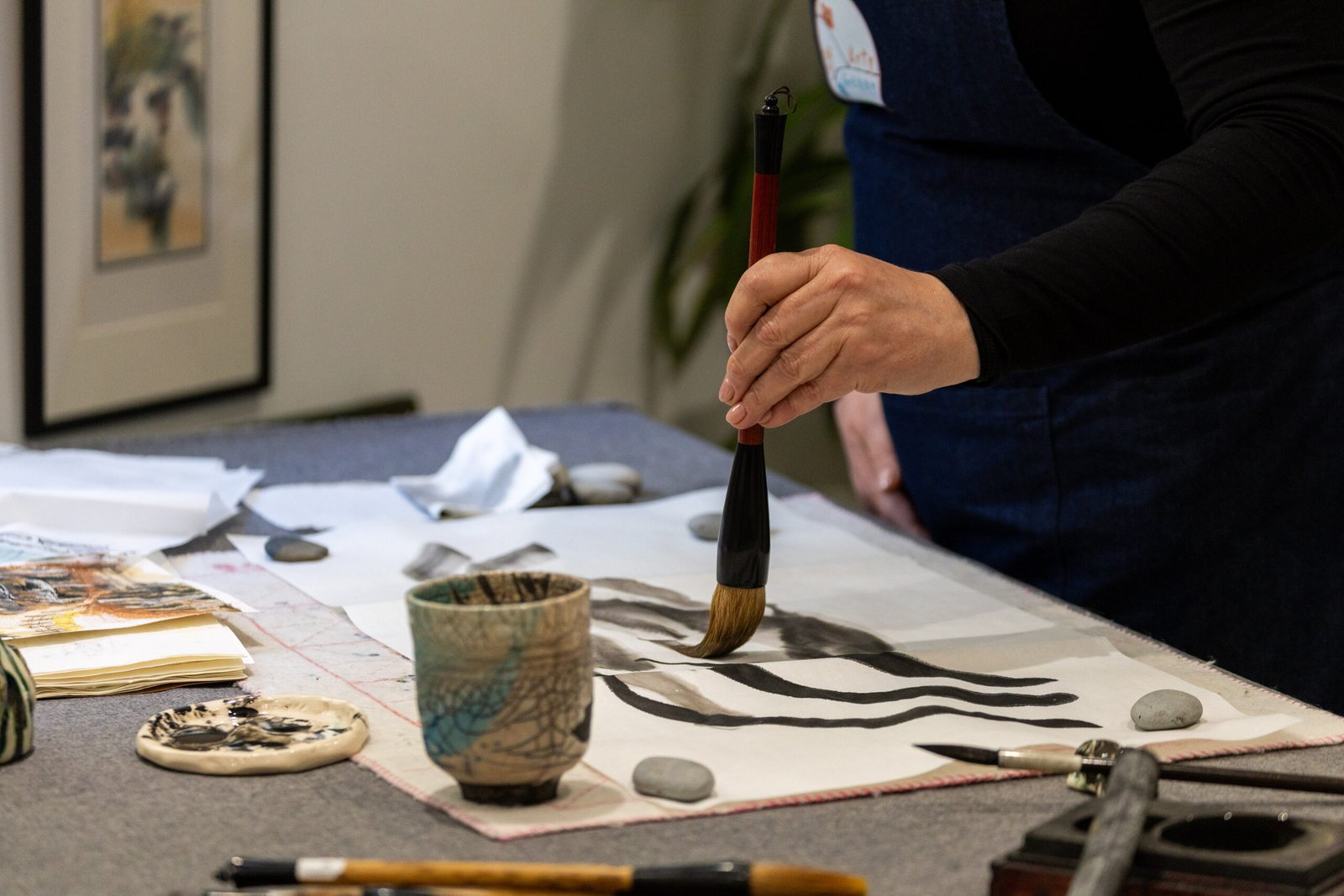 Genny's left hand holding a Chinese brush and painting mindful strokes with Chinese black ink onto Xuan paper