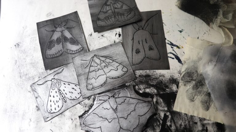 Inked Tetra Pak plates incised with various moth designs strewn on a messy, inky table
